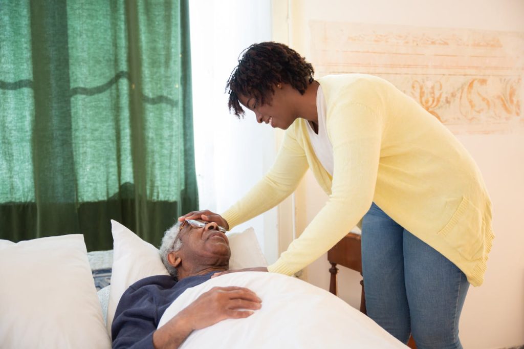 woman-touching-elderly-mans-head-7551684 A loving daughter tends to her elderly father at home, offering comfort and care.